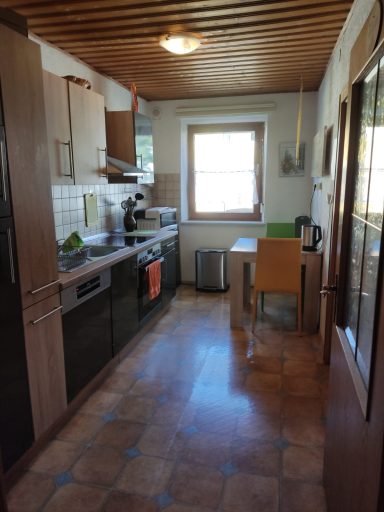 Helle Küche mit Holzdecken, moderner Ausstattung und Tisch neben einem Fenster.